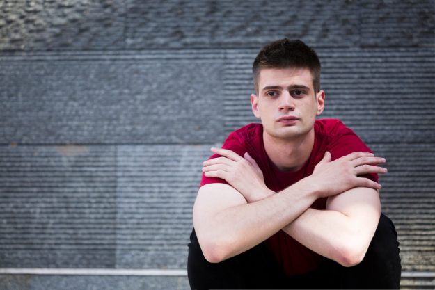 wistful-male-teenager-sitting-on-ground-with-arms-crossed